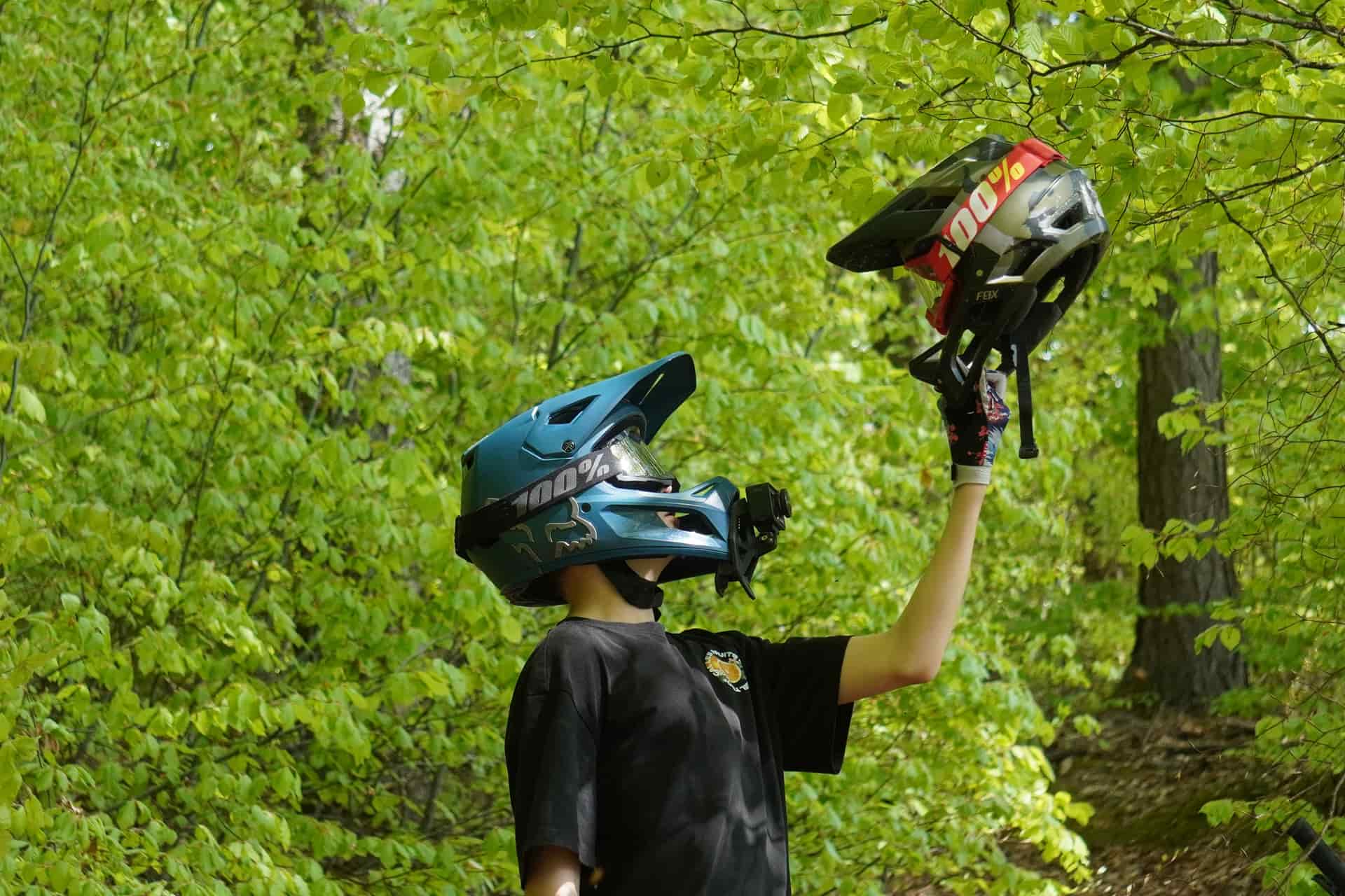 A mountain biker in a forest, holding a helmet
