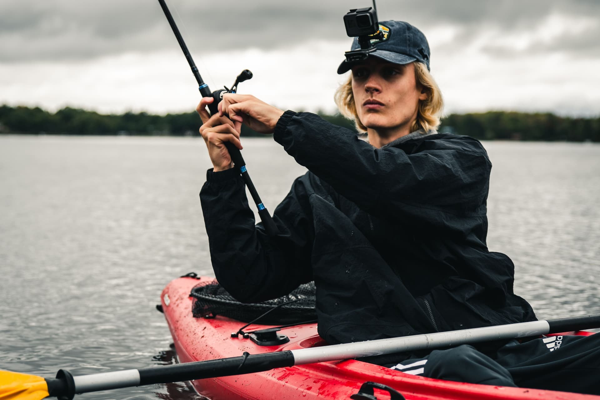 A man fishing from a kayak with an action camera on his cap