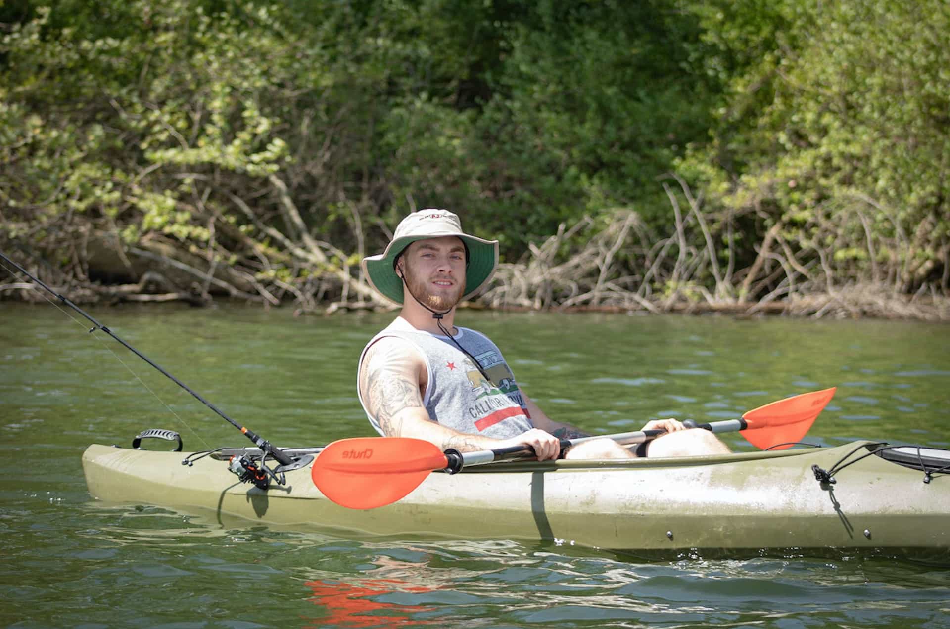 A man kayaking and fishing on a sunny river