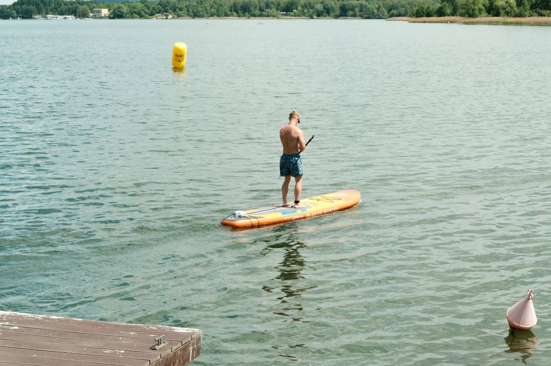 A lone paddle boarder standing on a board on a calm, sunlit lake